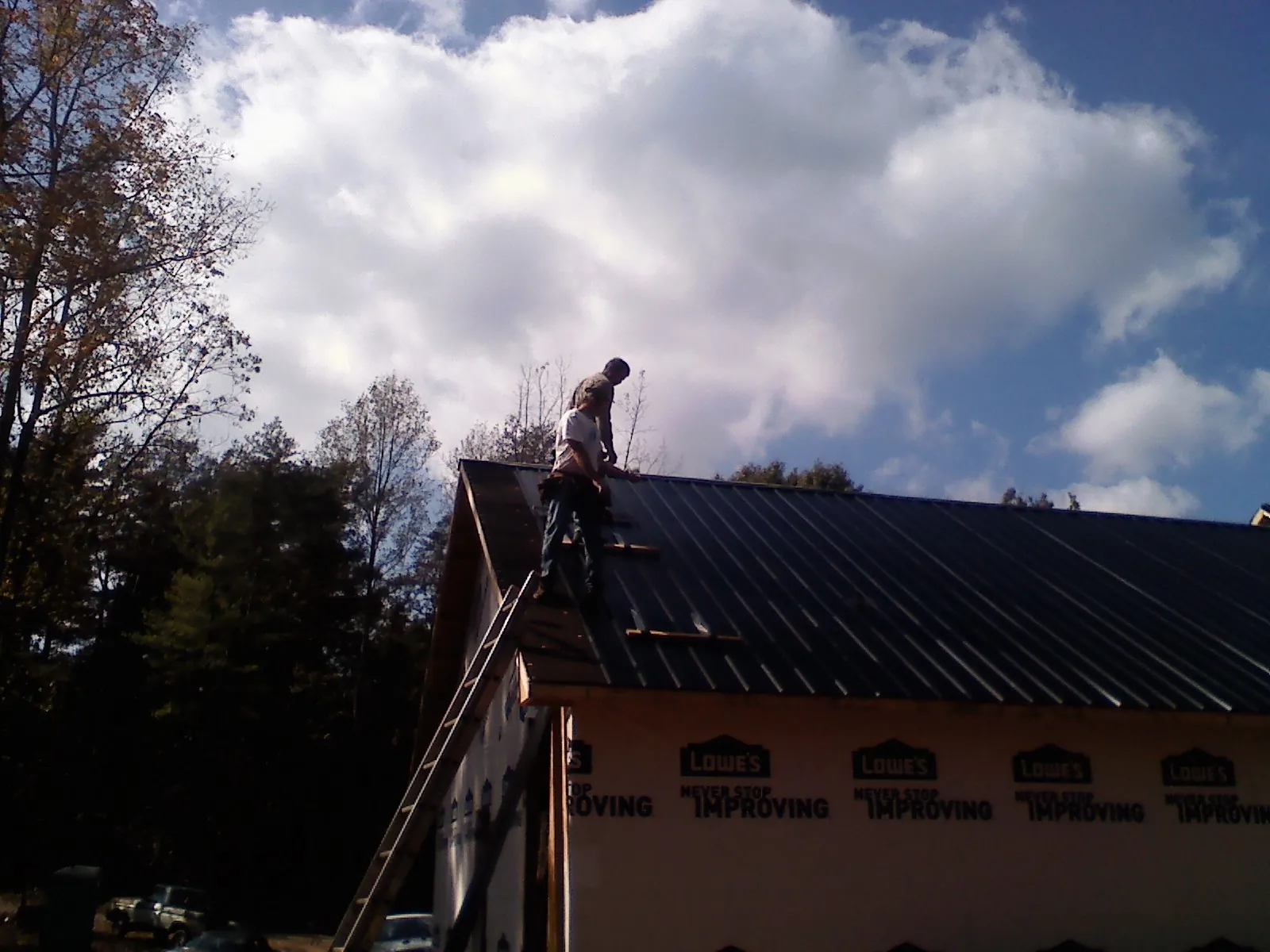 Roofer fastening dark metal panels high against a cloudy sky, from a Roof Inspection job in Bullhead City