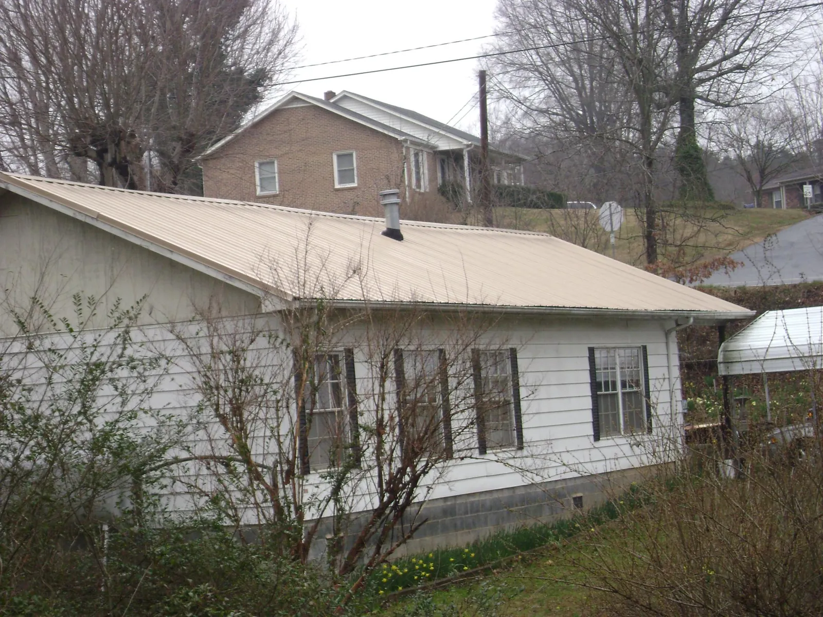 Tan metal roof on a white sided house set into a hillside — Commercial Roofing by Roofing Brothers in Bullhead City